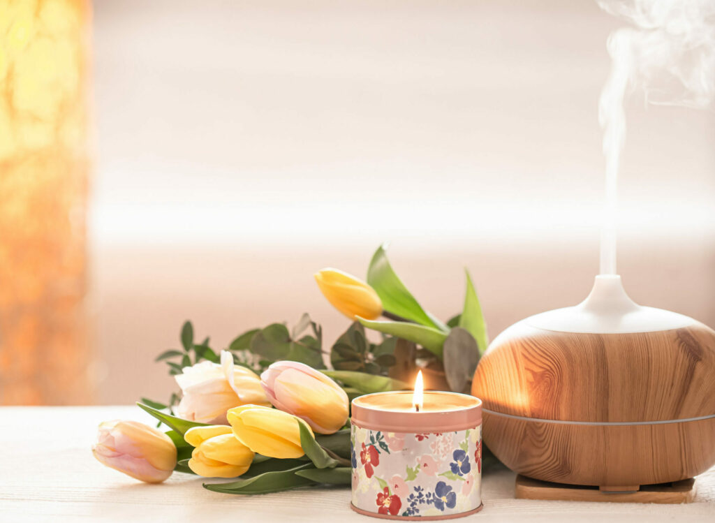 Aromatic oil diffuser lamp on the table on a blurred background with a beautiful spring bouquet of tulips and burning candles .